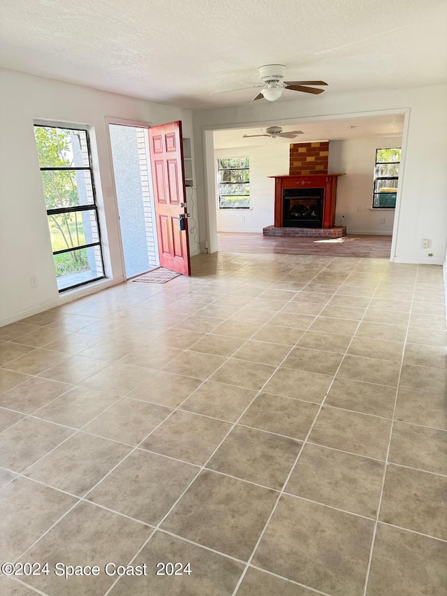 unfurnished living room featuring ceiling fan, a brick fireplace, plenty of natural light, and a textured ceiling