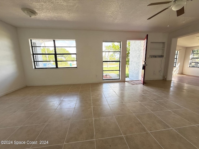 tiled spare room featuring ceiling fan, a textured ceiling, and plenty of natural light