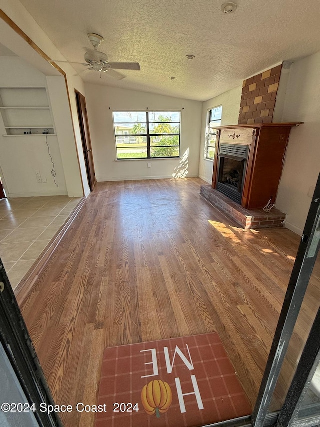 unfurnished living room featuring ceiling fan, lofted ceiling, a brick fireplace, a textured ceiling, and hardwood / wood-style floors