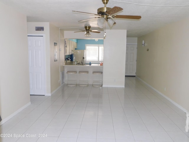 empty room with a textured ceiling, light tile patterned flooring, and ceiling fan