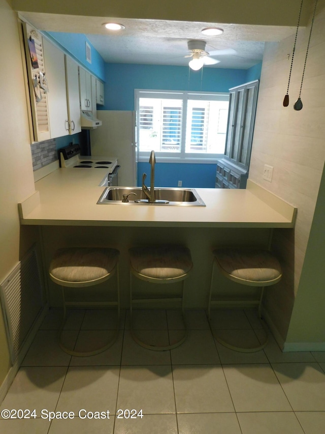 kitchen with white electric range, a peninsula, visible vents, under cabinet range hood, and a sink