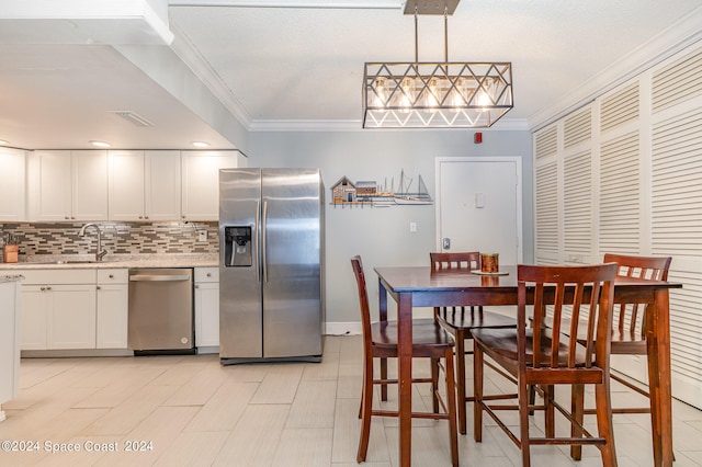 kitchen with stainless steel appliances, crown molding, sink, pendant lighting, and white cabinets