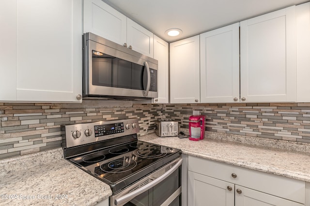 kitchen featuring appliances with stainless steel finishes, white cabinetry, light stone counters, and backsplash