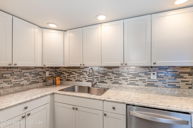 kitchen with backsplash, sink, stainless steel dishwasher, white cabinetry, and light stone counters