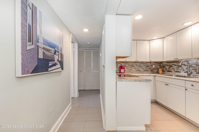 kitchen with white cabinets, tasteful backsplash, black electric cooktop, sink, and light stone counters