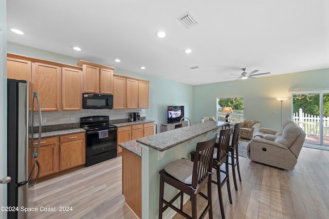 kitchen with a healthy amount of sunlight, black appliances, light hardwood / wood-style floors, and a kitchen breakfast bar