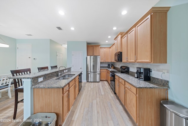 kitchen featuring a kitchen breakfast bar, light hardwood / wood-style floors, light stone countertops, black appliances, and sink