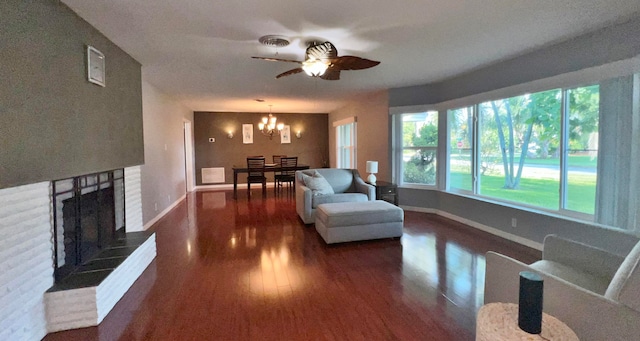 living room featuring ceiling fan with notable chandelier, a fireplace, and dark wood-type flooring