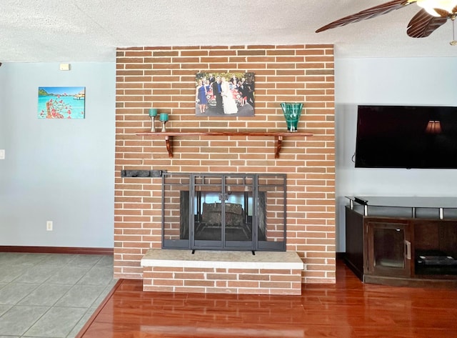 unfurnished living room with a textured ceiling, wood-type flooring, ceiling fan, and a brick fireplace