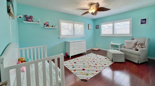 bedroom with ceiling fan, a crib, dark wood-type flooring, and multiple windows