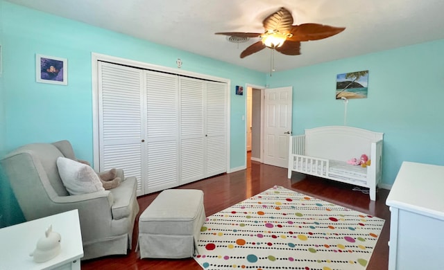 bedroom with ceiling fan, a nursery area, a closet, and dark wood-type flooring