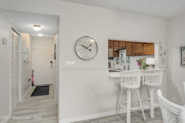 kitchen with sink, kitchen peninsula, a textured ceiling, a breakfast bar, and light wood-type flooring