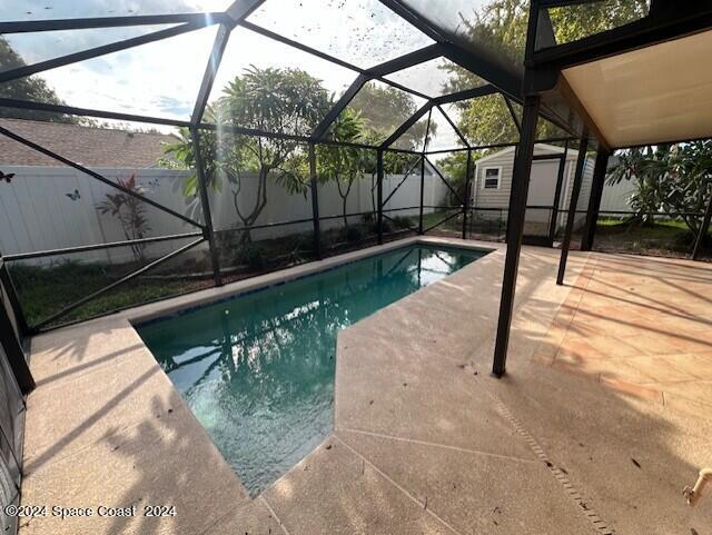 view of swimming pool with glass enclosure, a storage unit, and a patio