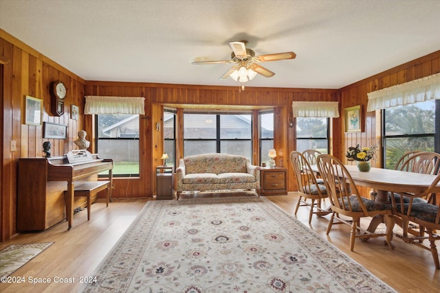 dining space with ceiling fan, wooden walls, light wood-type flooring, and ornamental molding