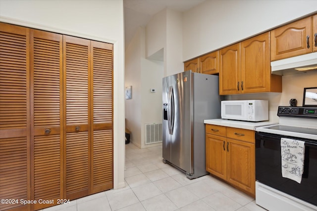 kitchen featuring a towering ceiling, light tile patterned floors, and white appliances