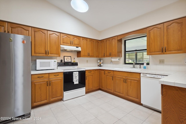 kitchen with sink, tile countertops, vaulted ceiling, and white appliances