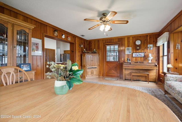 dining space featuring ceiling fan, light hardwood / wood-style floors, wooden walls, and ornamental molding