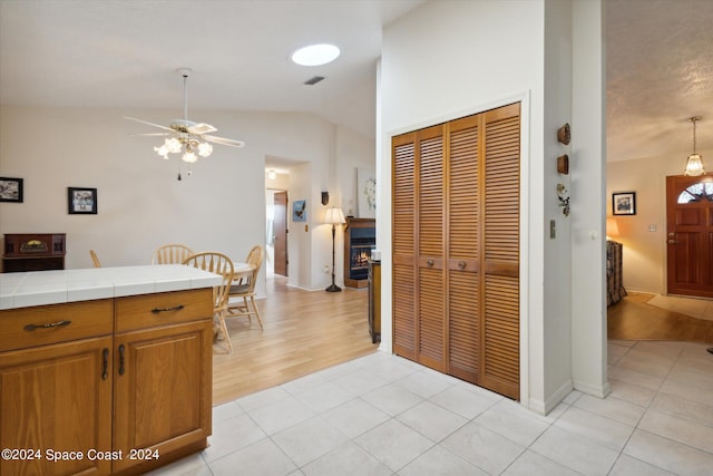 kitchen with ceiling fan, tile countertops, light hardwood / wood-style floors, and lofted ceiling