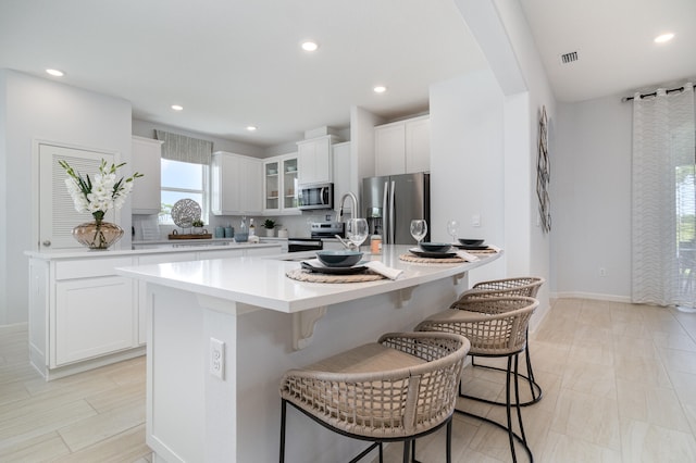 kitchen with a kitchen breakfast bar, white cabinetry, appliances with stainless steel finishes, and a center island