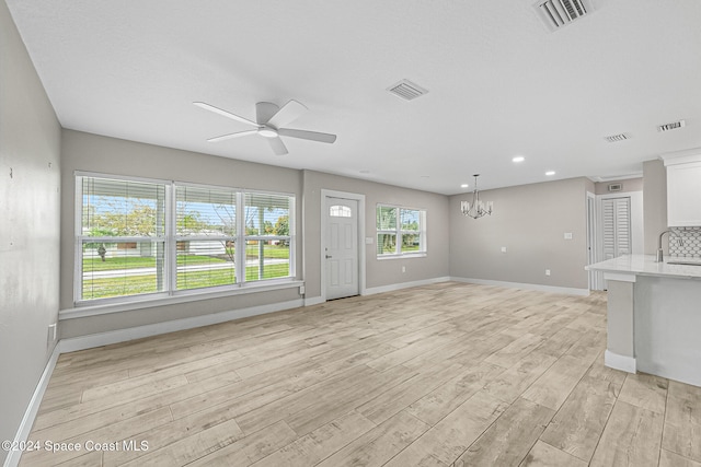 unfurnished living room featuring sink, ceiling fan with notable chandelier, and light wood-type flooring