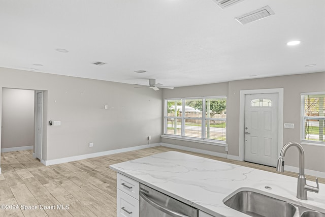 kitchen featuring white cabinets, light stone countertops, light wood-type flooring, dishwasher, and sink