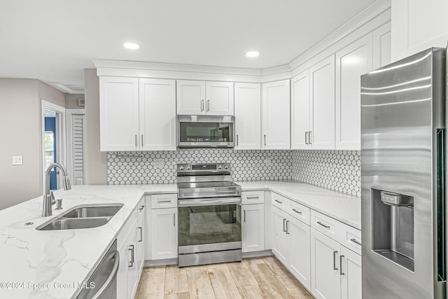 kitchen featuring appliances with stainless steel finishes, sink, light stone countertops, white cabinetry, and light hardwood / wood-style floors