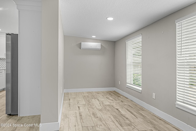 empty room featuring light wood-type flooring, a textured ceiling, and a wall mounted air conditioner