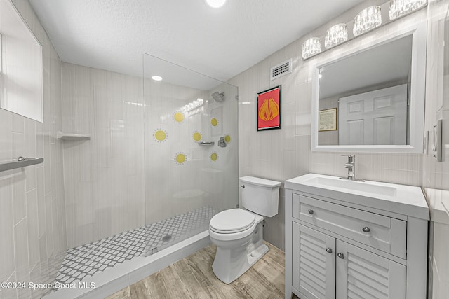 bathroom featuring toilet, vanity, wood-type flooring, and tiled shower