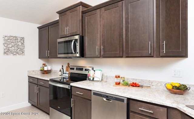 kitchen featuring dark brown cabinetry, light stone countertops, stainless steel appliances, and light tile patterned floors