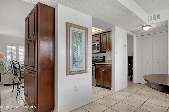 kitchen with appliances with stainless steel finishes, a textured ceiling, and light tile patterned flooring