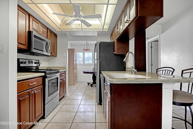 kitchen featuring sink, a breakfast bar area, ceiling fan, stainless steel appliances, and light tile patterned floors