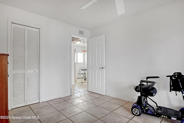 workout room with ceiling fan, a textured ceiling, and light tile patterned floors