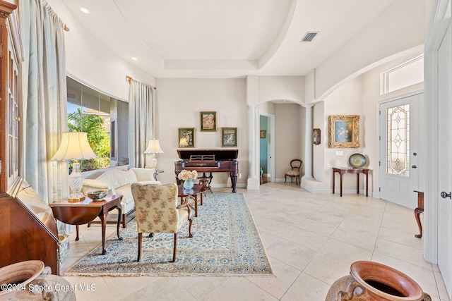 living area with decorative columns, a raised ceiling, plenty of natural light, and light tile patterned floors