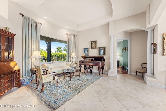 living area featuring a raised ceiling, ornate columns, a towering ceiling, and light tile patterned floors