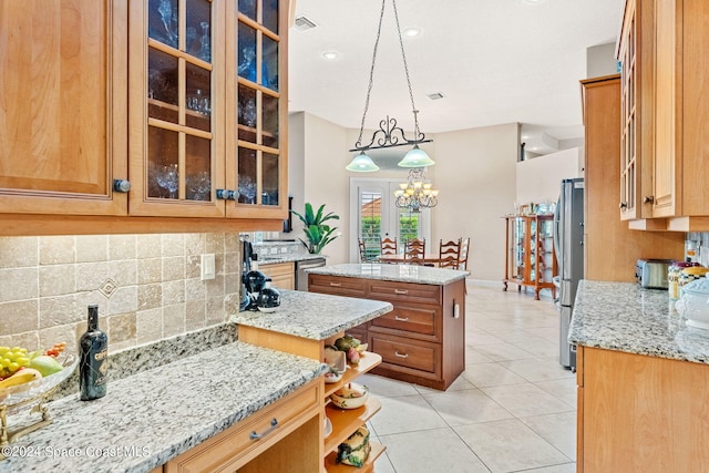 kitchen featuring stainless steel refrigerator, light stone counters, a center island, and decorative light fixtures