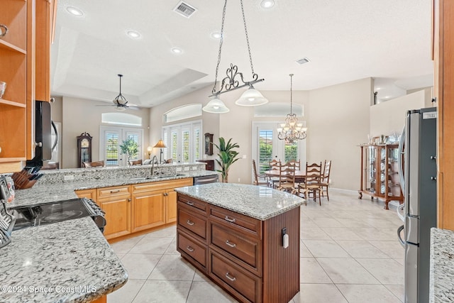 kitchen with ceiling fan with notable chandelier, a raised ceiling, sink, appliances with stainless steel finishes, and a kitchen island