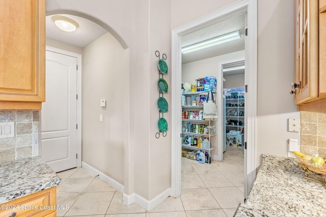 interior space with light tile patterned flooring, light stone countertops, a textured ceiling, and tasteful backsplash