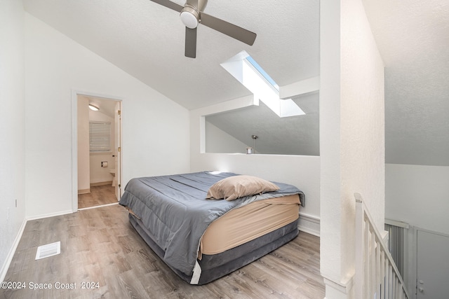 bedroom with light hardwood / wood-style floors, a textured ceiling, connected bathroom, lofted ceiling with skylight, and ceiling fan