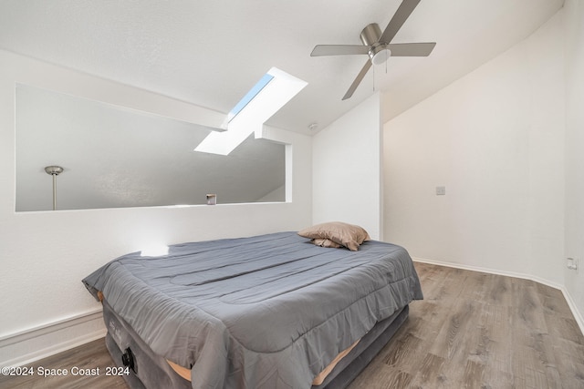 bedroom featuring wood-type flooring, vaulted ceiling with skylight, and ceiling fan