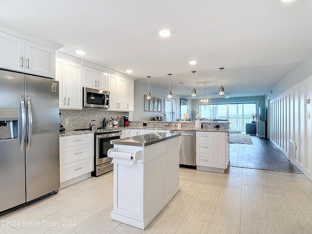 kitchen featuring white cabinets, kitchen peninsula, a kitchen island, stainless steel appliances, and decorative light fixtures