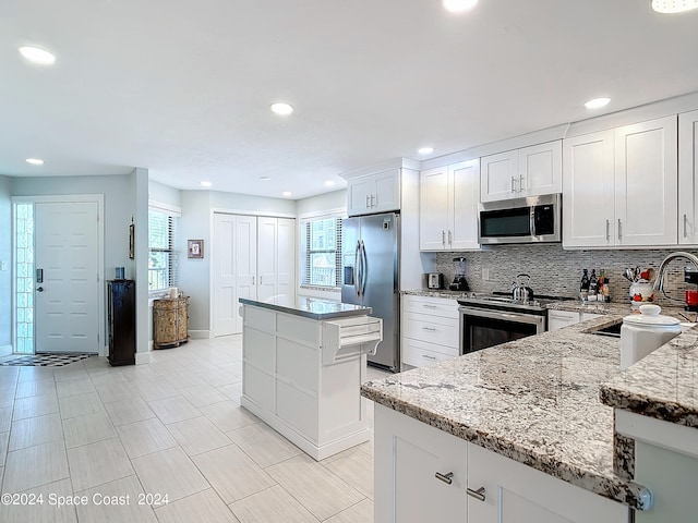 kitchen featuring a healthy amount of sunlight, stainless steel appliances, white cabinetry, and a kitchen island