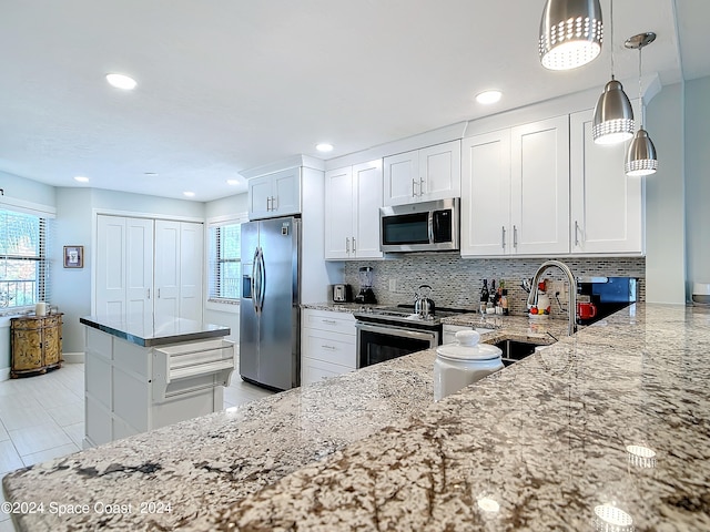 kitchen featuring light stone counters, sink, white cabinets, appliances with stainless steel finishes, and decorative light fixtures