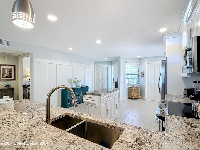 kitchen with sink, white cabinets, appliances with stainless steel finishes, decorative light fixtures, and light stone countertops