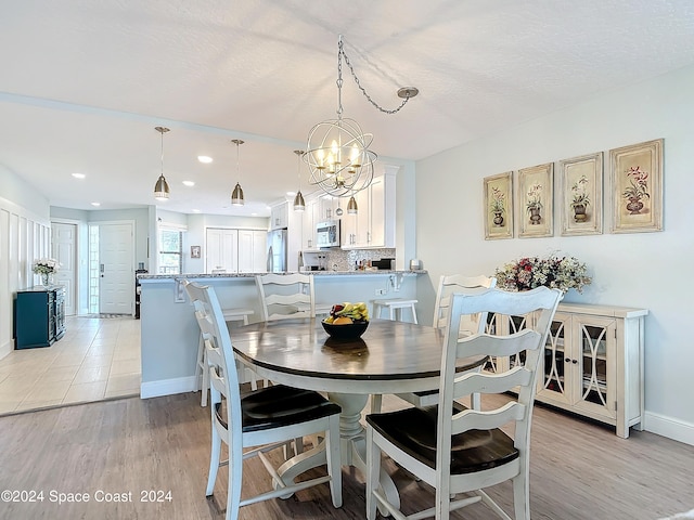 dining space featuring an inviting chandelier, light wood-type flooring, and a textured ceiling