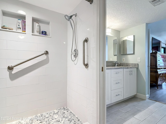 bathroom with vanity, hardwood / wood-style floors, a textured ceiling, and tiled shower