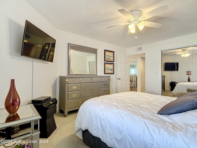 bedroom featuring ceiling fan, light colored carpet, a textured ceiling, and a closet