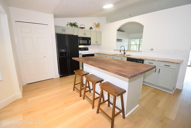 kitchen with black appliances, backsplash, wood counters, vaulted ceiling, and a breakfast bar area