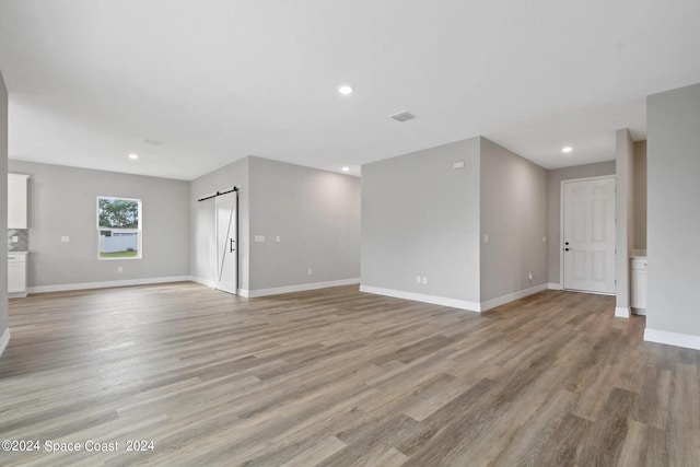 unfurnished living room with a barn door and light wood-type flooring