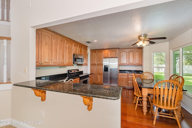 kitchen with stainless steel appliances, kitchen peninsula, hardwood / wood-style flooring, and a textured ceiling