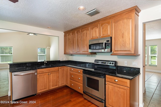 1290 Mercedes Dr, Merritt Island, FL 32952 - kitchen featuring appliances with stainless steel finishes, a sink, a textured ceiling, dark stone counters, and a peninsula